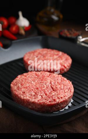 Rohe Hamburger-Pasteten mit Öl auf der Grillpfanne, Nahaufnahme Stockfoto