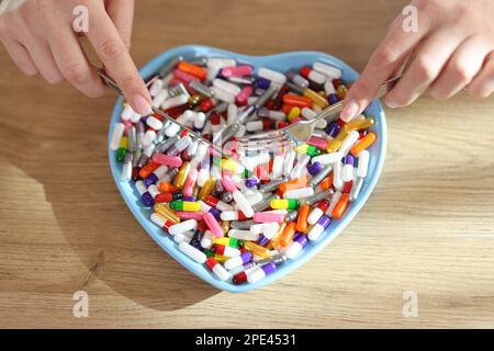 Frauenhände halten Messer und Gabel über herzförmigen Teller mit einem Haufen verschiedener Pillen. Stockfoto