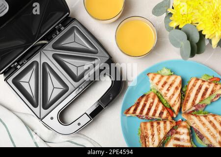 Moderne Grillmaschine, Saft und Sandwiches auf einem weißen Tisch, flach liegend Stockfoto