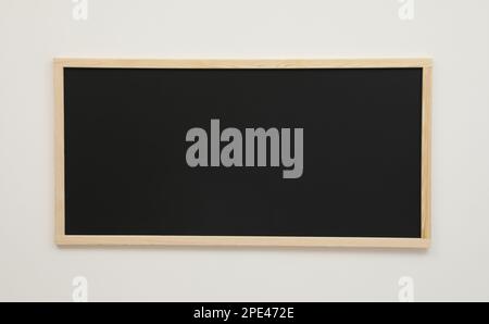 Saubere schwarze Tafel, die an der weißen Wand hängt Stockfoto