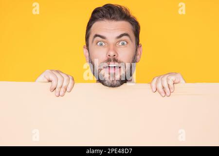 Ein gut aussehender Mann, der ein leeres Brett hält und mit dem Finger auf den Studiohintergrund zeigt. Erstaunlicher Typ, der ein leeres Schild mit Werbeträger zeigt. Idee und Angebot Stockfoto