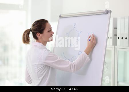 Glückliche Wissenschaftlerin, die chemische Formeln auf dem Whiteboard zeichnet. Stockfoto