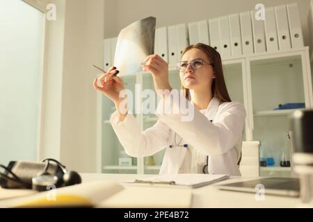 Ein Arzt mit ernstem Gesicht schaut auf die Röntgenaufnahme, während er am Tisch in der medizinischen Klinik sitzt. Stockfoto