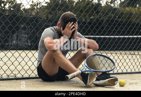 Trauriger Sportler, der auf dem Tennisplatz saß und nach dem verlorenen Spiel weinte. Stockfoto