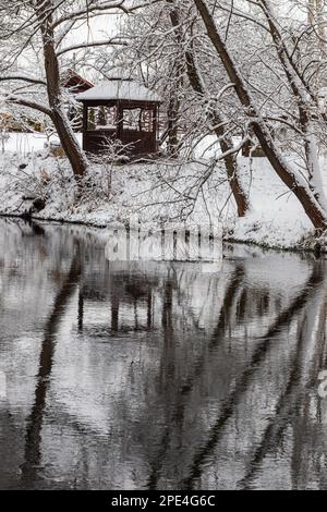 Ein kleiner hölzerner Pavillon in den Tiefen eines Winterwaldes in der Nähe eines kalten Gebirgsbachs, an dem ertrunkene Menschen vorbeigehen und aus einem Waldtal hochklettern. Stockfoto