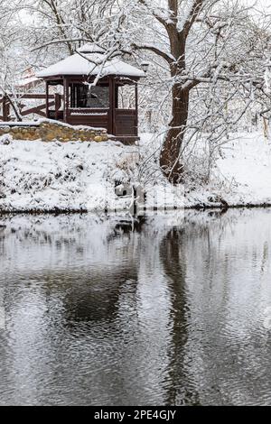 Ein kleiner hölzerner Pavillon in den Tiefen eines Winterwaldes in der Nähe eines kalten Gebirgsbachs, an dem ertrunkene Menschen vorbeigehen und aus einem Waldtal hochklettern. Stockfoto