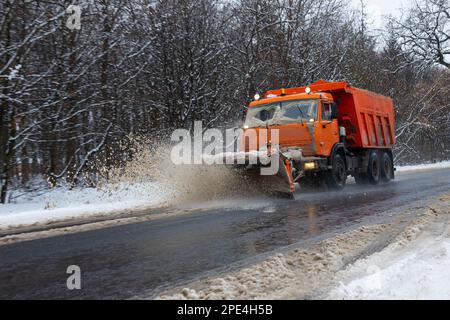 Ein großes Auto mit einem Pflug befreit die Straße von Schnee. Die Sonderausrüstung Orange Cargo kämpft im Winter mit den Elementen. Beseitigung der Auswirkungen von t Stockfoto