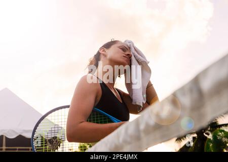 Sportlerin, die sich nach dem Tennisspiel mit einem Handtuch das Gesicht abwischt. Stockfoto