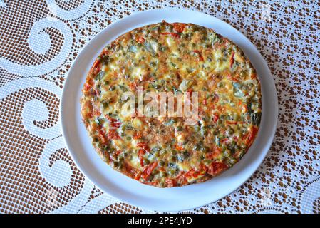 Eine italienische Frittata aus Eiern, Fleisch, Käse und Gemüse auf einem Teller mit weißer Tischdecke. Ein frisches, köstliches und gesundes Essen Stockfoto