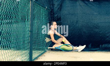 Eine traurige und müde Tennisspielerin sitzt nach einem Spiel auf dem Tennisplatz. Stockfoto
