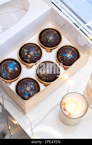 Schokoladenkugeln in goldener Geschenkbox mit brennender Kerze Stockfoto