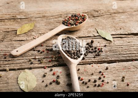 Mischung aus Paprika und Erbsen in einem Holzlöffel auf Holzhintergrund, Draufsicht. Roter Pfeffer, weißer Pfeffer und grüner Pfeffer. Stockfoto