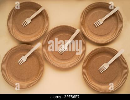 Fünf handgefertigte Einwegteller mit Holzgabel auf beigem Hintergrund. Draufsicht. Biologisch abbaubares Konzept und Erhaltung der natürlichen Ressourcen. Stockfoto