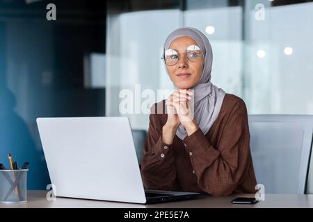 Portrait einer erfolgreichen und selbstbewussten muslimischen Frau im Hijab. Regisseur, Besitzer, Geschäftsfrau, die im Büro mit einem Laptop sitzt. Stockfoto