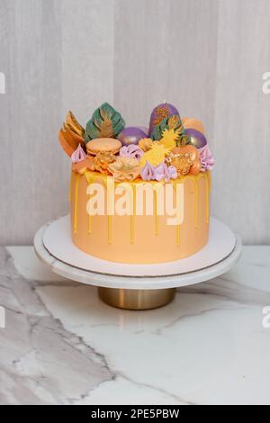 Zarte Korallen und Orangen mit geschmolzener Schokolade, Makronen, Kuchenpops und Süßigkeiten auf Marmorkakestand. Grauer Hintergrund Stockfoto