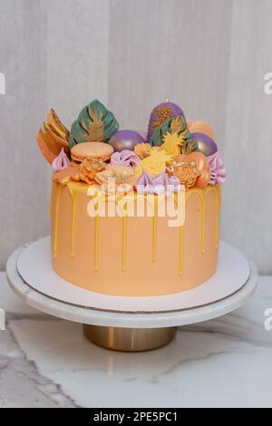 Zarte Korallen und Orangen mit geschmolzener Schokolade, Makronen, Kuchenpops und Süßigkeiten auf Marmorkakestand. Grauer Hintergrund Stockfoto