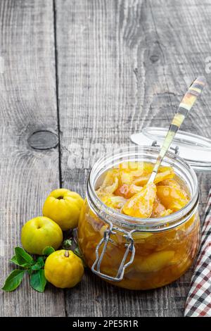 Hausgemachte Quittenmarmelade in Glasgefäßen und frische Quitten mit Blättern auf einem Holztisch Stockfoto