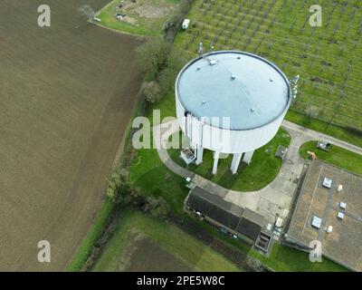 Luftaufnahme eines großen Wasserturms aus Beton neben einem großen Schuppen, in dem Hühner untergebracht sind. Im Hintergrund ist ein Obstgarten zu sehen. Stockfoto