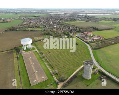 Blick auf die Drohne auf einen großen Wasserturm aus Beton auf der linken Seite neben einem riesigen Hühnerschuppen. Auf einem grauen Wasserturm ist eine fast 5G:1-Anordnung zu sehen. Stockfoto
