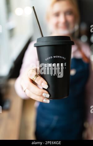 Barista Girl hält ein schwarzes Metallglas mit der Aufschrift Good Morning Lieblingskaffee in den Händen mit zubereitetem heißem Kaffee. Professionell c Stockfoto