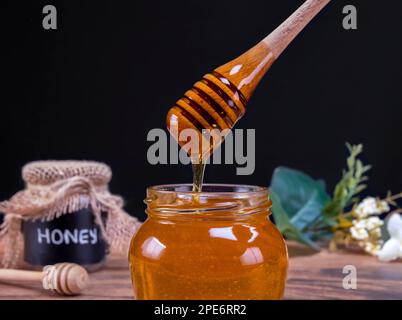 Honiglöffel, der in Zeitlupe aus dem Glas mit Honig kommt. Honig enthält viele Nährstoffe, Antioxidantien, verbessert die Gesundheit des Herzens, Wundversorgung, Angebote Stockfoto