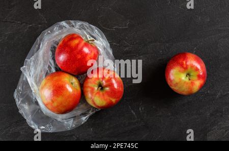 Vier rote Äpfel mit Plastiktüte aus dem Supermarkt auf einem schwarzen schieferähnlichen Tisch, Blick von oben Stockfoto