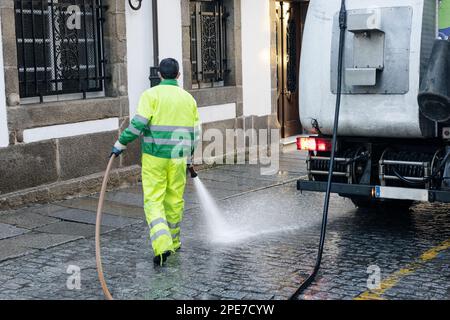 Arbeiter reinigen mit Druckwasser eine Straße einer historischen Stadt. Städtisches Instandhaltungskonzept Stockfoto