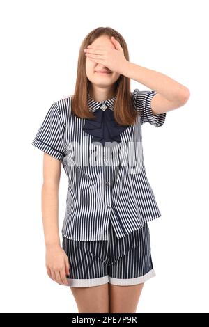 Ein junges, schönes Mädchen in Schuluniform auf weißem Hintergrund, lächelt und lacht, mit der Hand im Gesicht, das die Augen für eine Überraschung verdeckt. Blindes Konzept. Stockfoto