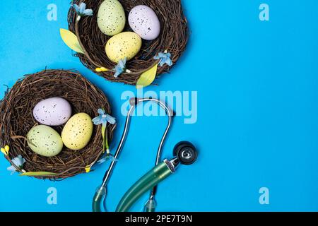 Ostermedizin. Zwei Nester mit lackierten Eiern und ein Stethoskop auf blauem Hintergrund, Platz für Text Stockfoto