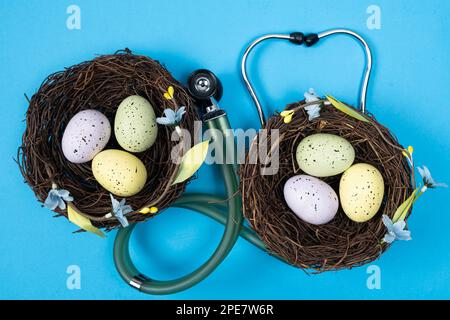 Ostermedizin. Zwei Nester mit bemalten Eiern und ein Stethoskop auf blauem Hintergrund Stockfoto