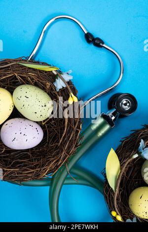 Ostermedizin. Zwei Nester mit bemalten Eiern und ein Stethoskop auf blauem Hintergrund Stockfoto