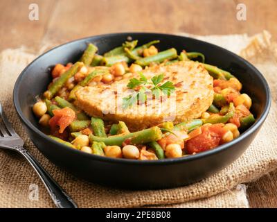 Grüne Bohnen und Tomateneintopf mit Kichererbsen und veganem Kotelett Stockfoto