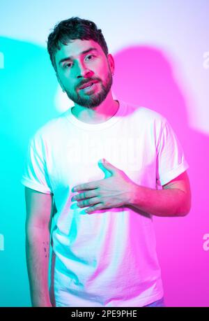 Künstlerisches kreatives Porträt, bärtiger Mann mittleren Alters in weißem T-Shirt mit leuchtendem Neonhintergrund. Zweifarbige Schatten. Ein moderner, gut aussehender Mann Stockfoto