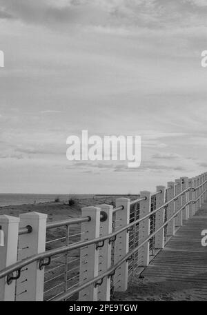 Am Salisbury Beach, Massachusetts, erhebt sich eine leere Promenade über dem Strand und der Küste, während die Sonne untergeht. Das Bild wurde in analogem Schwarzweiß aufgenommen Stockfoto