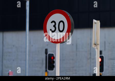 Straßenschild am Stab mit Geschwindigkeitsbegrenzung von 30 km, mit Ampeln im Hintergrund, Christchurch, Neuseeland. Stockfoto