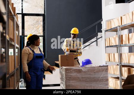 afroamerikanische Lagerarbeiter, die Verpackungen für den Versand verpacken. Alle Mitarbeiter der schwarzen Lieferabteilung bereiten Pakete für den Transport vor und verwenden Klebebandabroller Stockfoto