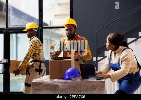 Lagermitarbeiter überprüfen Bestelllisten auf Laptops und Paketen. Ein afrikanisches Lagerteam bereitet Waren für den Versand im Lagerraum vor Stockfoto