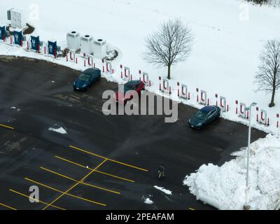 Ein hohes Luftbild mit drei geparkten Tesla Elektrofahrzeugen an einer Tesla Supercharger Station im Winter. Stockfoto