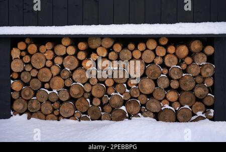 Brennholz unter dem Haus bei Schneewetter gestapelt Stockfoto