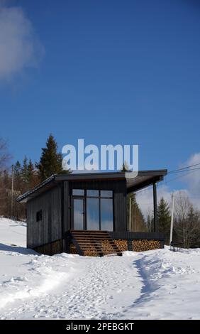 Vorderansicht einer modernen Holzhütte auf schneebedeckten Bergen Stockfoto