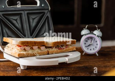 Sandwiches mit Käse, Würstchen und Oliven in einem Sandwichmaker auf Holzhintergrund zubereiten. Stockfoto