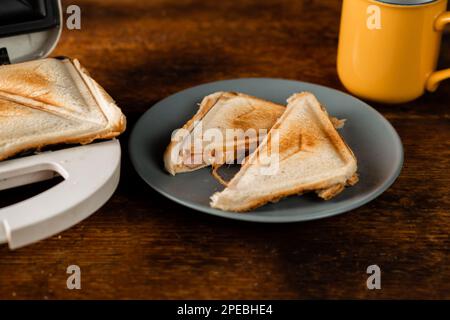 Frisch getoastete Sandwiches von einem Sandwichmaker auf einem Teller mit rustikalem Holzhintergrund. Getoastete dreieckige Sandwiches mit Käse.