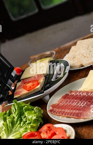 Sandwichmaker und verschiedene Zutaten auf Holzhintergrund. Ich koche Sandwiches. Stockfoto