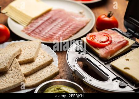 Sandwichmaker und verschiedene Zutaten auf Holzhintergrund. Ich koche Sandwiches. Stockfoto