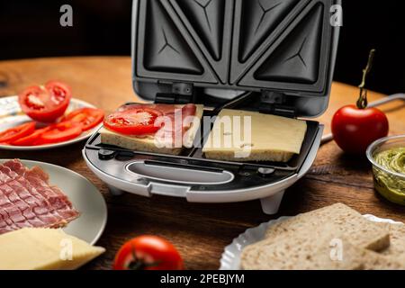 Sandwichmaker und verschiedene Zutaten auf Holzhintergrund. Ich koche Sandwiches. Stockfoto