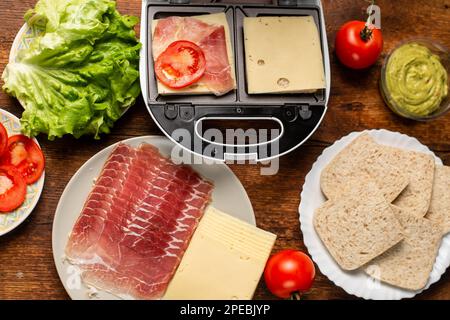 Sandwichmaker und verschiedene Zutaten auf Holzhintergrund. Ich koche Sandwiches. Stockfoto