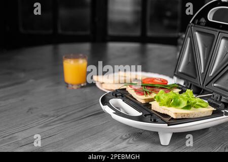 Köstliche Sandwiches mit Schinken und Kräutern in einem Sandwichmaker auf schwarzem und weißem Hintergrund. Stockfoto