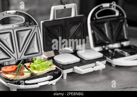 Köstliche Sandwiches mit Schinken und Kräutern in einem Sandwichmaker auf schwarzem und weißem Hintergrund. Stockfoto