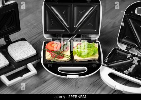 Köstliche Sandwiches mit Schinken und Kräutern in einem Sandwichmaker auf schwarzem und weißem Hintergrund. Stockfoto