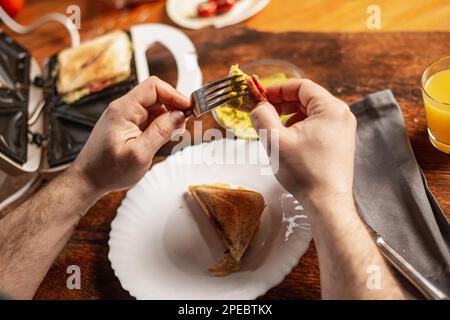 Ein unbekannter Mann isst Toast mit Guacamole. Frühstückszeit. Die Hände des Mannes halten einen Toast. Stockfoto